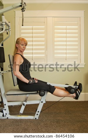 Attractive blond woman using exercise machine for leg lifts