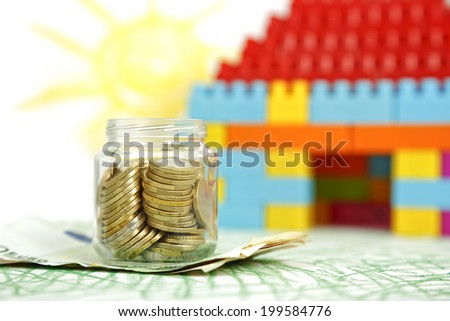 jar of coins in front of house of blocks