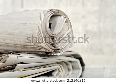 rolled newspaper on stack of newspapers against blurry background