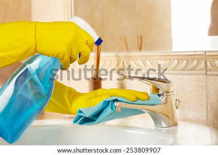 woman in rubber gloves with rag and detergent cleaning the bathroom