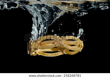 elaborate gold bracelet splashing in water against black
