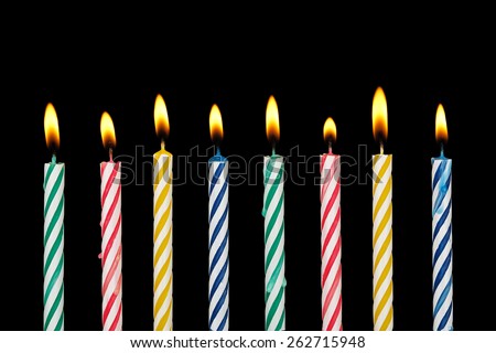 eight colorful birthday candles with flame on black