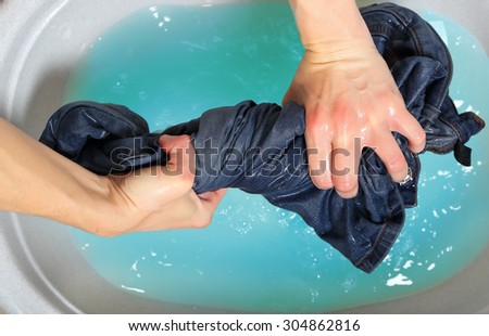 woman washing a pair of jeans by hand in plastic tub