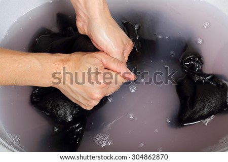 woman washing delicate clothes by hand in plastic tub