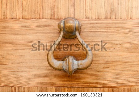 Brass door knocker hanging on a wooden door for gaining access or entry by creating a noise