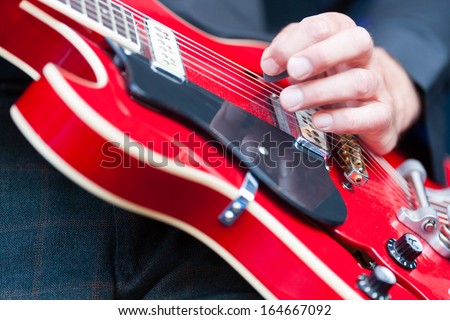 Close up of the hand of a man playing an electric guitar plucking the strings with his fingers during a live performance with a band or orchestra