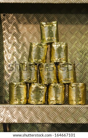 Old battered tin cans stacked in a pyramid on a metal shelf as a decoration or target