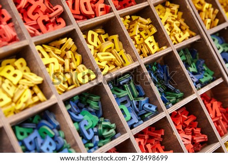 Large collection of colorful plastic alphabet letters stored in a wooden box with square compartments for teaching kids to read and spell, overhead viewful alphabet letters
