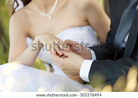 At the wedding, the groom puts the ring on the bride\'s finger. Hand of the groom and the bride with wedding rings at a wedding party . Outdoors