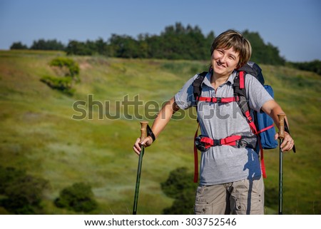Traveler with a backpack and hiking sticks. Woman traveler looking straight and smiling.  Photographed in Russia. Photographed in Russia.