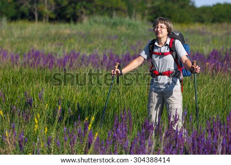 Traveler with a backpack and hiking sticks. The girl is a traveler on the meadow with flowers. Photographed in Russia.