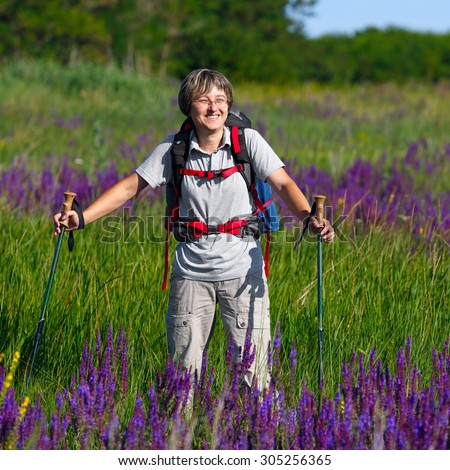 Traveler with a backpack and hiking sticks. Woman traveler looking straight and smiling.The girl  on the meadow with flowers.  Photographed in Russia.
