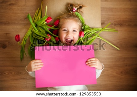 Funny blond girl lying on floor with flowers and pink paper card