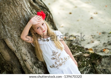 Pretty european blond girl sitting on huge tree in tropical garden