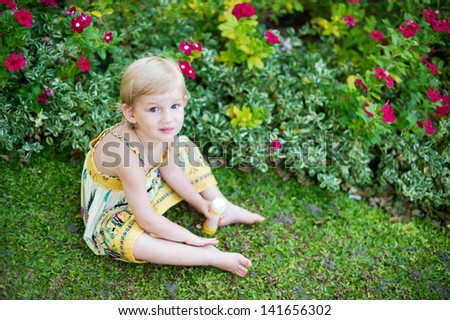 Adorable little girl in dress sitting in tropical blooming garden plays with flowers