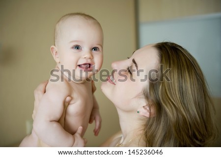 Happy young mother holding her newborn baby boy skin to skin and playing with him
