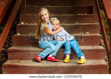 Two adorable european sisters holding each other and sitting on stairs in autumn park