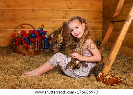 Beautiful happy girl with long blond hair playing with funny easter rabbit in hay in country house
