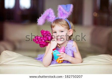 Happy funny little girl with colorful pink flowers and fancy bunny ears on head celebrates easter. Toy han in hands.