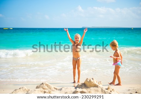 Two cute little sisters girls having fun on colorful tropical beach with turquoise water of ocean and white sand