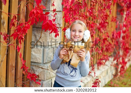 Very beautiful model toddler girl stay at colorful autumn street and enjoy chocolate bars. Red plants on background.