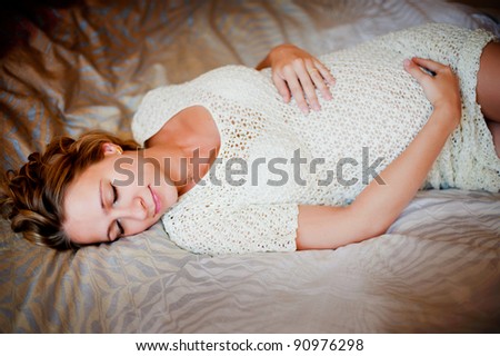 Beautiful pregnant woman having rest in white dress and holding her belly