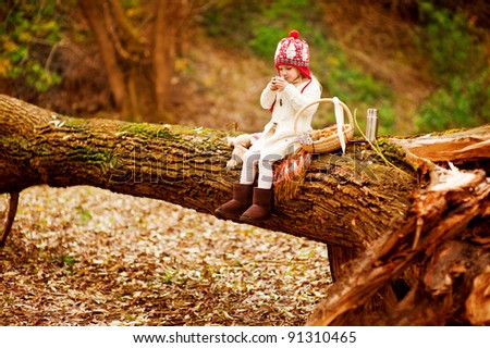 Little girl sitting on huge tree and drinking tea