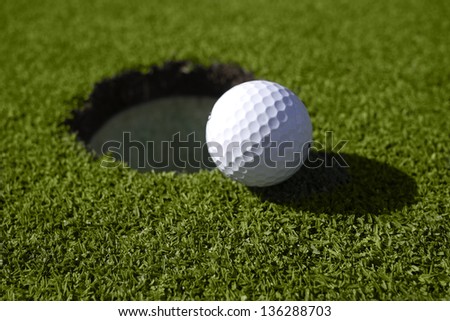 White golf ball lies right at the lip of the golf hole on the green.