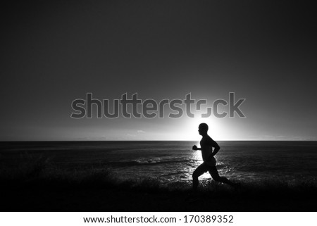 A silhouette of jogger at a grassy path along the ocean.  In black and white.