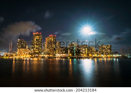 Long exposure image of full moon over Ala Wai Boat Harbor and Waikiki with Diamond Head in distant background.