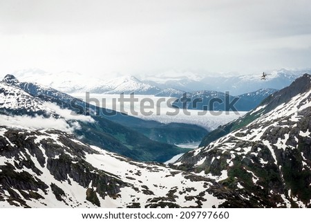 Helicopter flies over Alaska landscape of snow capped mountains,
