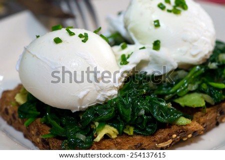 Poached egg on whole grain toast topped with avocado and spinach, seasoned with diced chives