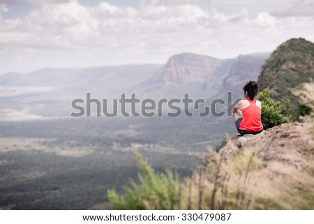 Young woman sitting at edge of cliff looking over expansive view of plains and mountains in South Africa