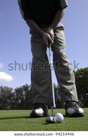 Golfer addresses a golf ball with a putter on the putting green.