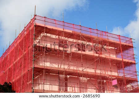 A building being renovated with scaffolding and covered in red tarpaulin.