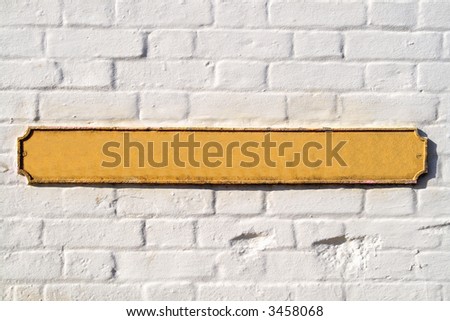 Blank yellow British street sign on a white wall.