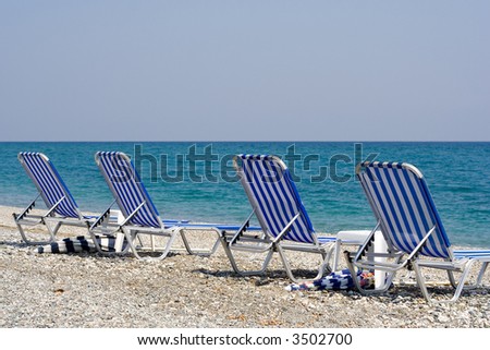 Four beach chairs in front of the ocean deep blue (the Aegean Sea in Greece)