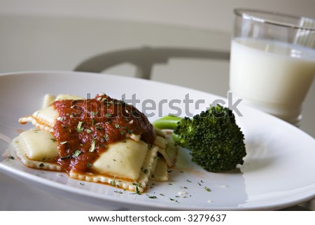 Ravioli with Red Sauce and a side of Steamed Broccoli set on a glass table, and Milk as the Beverage