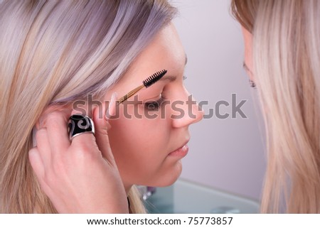 Stylist is applying eyebrow brush for young girl