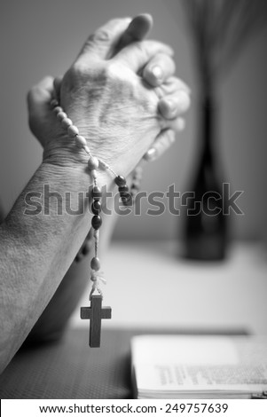 A woman prays to God. In the background holy bible and rosary. Black and white