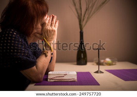 A woman prays to God. In the background holy bible and rosary