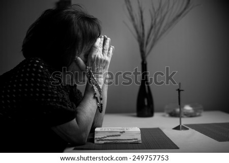 A woman prays to God. In the background holy bible and rosary. Black and white