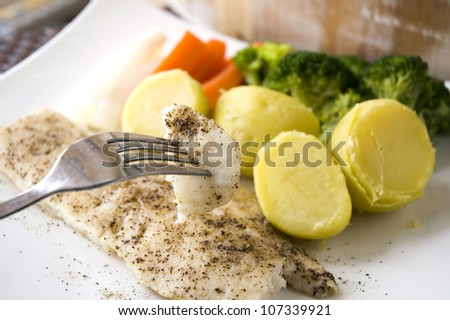 baked fish on fork with healthy food plate background