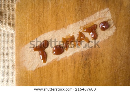 ketchup in tomato word on wooden cutting board