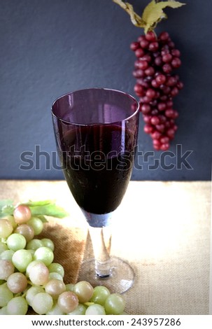 glass of red grape juice with grapes on background