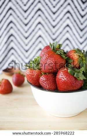 big bowl of fresh strawberry put on wooden table with black and white zigzag background
