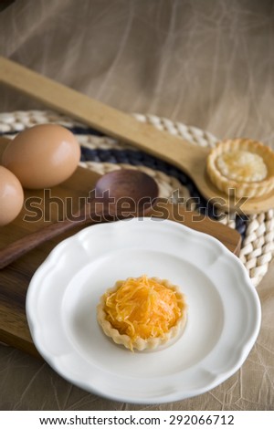 sweet mini golden tart on dish with eggs and wooden spoon on background