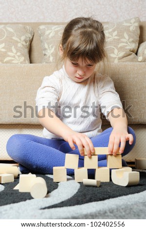 The little girl plays wooden toy cubes. A house room