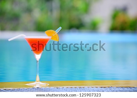 Cocktail at the edge of the swimming pool. Red cocktail with an orange slice on the background of the swimming pool