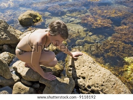 The girl on sitting squat looking something between stones at ocean